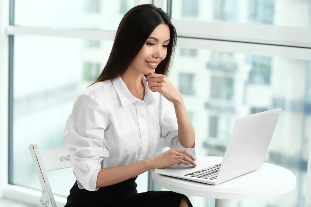 Mlada žena u beloj košulji analizira opcije na laptopu u svetlom kancelarijskom prostoru dok planira korake za izbor softvera
