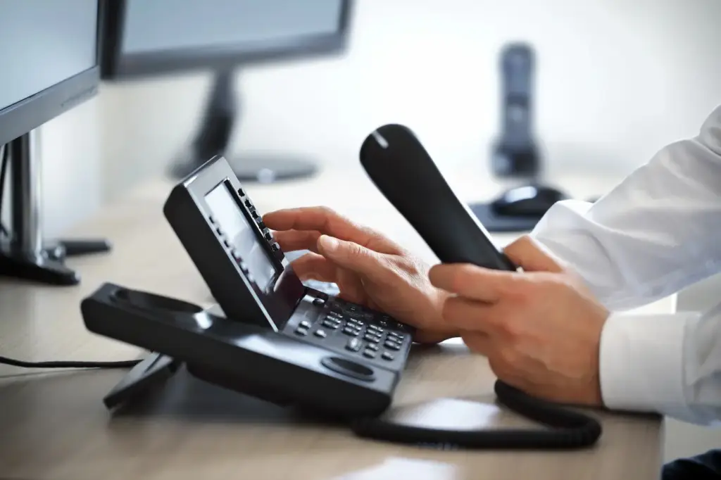Osoba drži telefonsku slušalicu i bira broj na modernom kancelarijskom telefonu