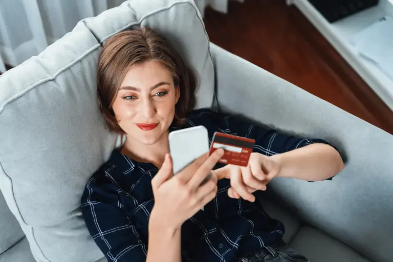 Krupni plan osobe koja drži pametni telefon i kreditnu karticu dok obavlja online transakciju i kupovinu u udobnom okruženju
