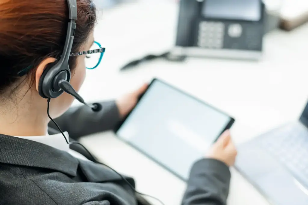 A business woman with a headset holds a digital tablet while sitting at a desk